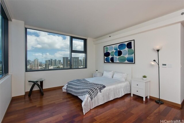 bedroom featuring a view of city, wood finished floors, and baseboards