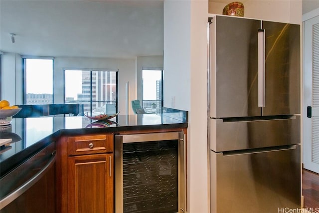 kitchen featuring stainless steel appliances, wine cooler, brown cabinetry, and dark countertops