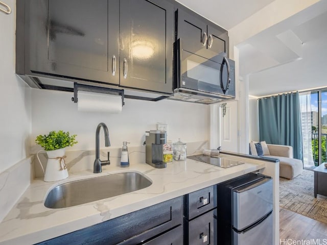 kitchen with light stone countertops, a sink, light wood-type flooring, floor to ceiling windows, and black appliances