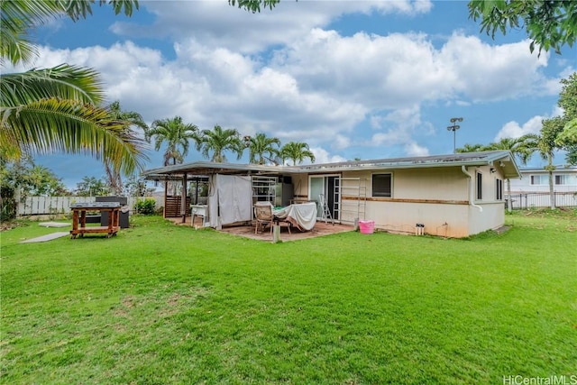 rear view of house featuring a yard, fence, and stucco siding