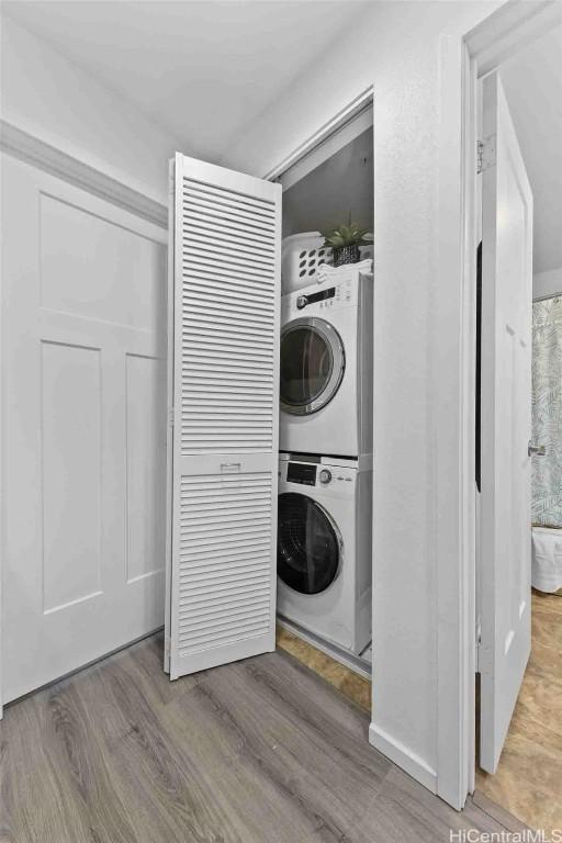 clothes washing area with light wood-type flooring, stacked washer / dryer, and laundry area