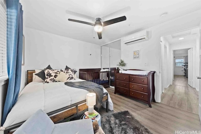 bedroom with ceiling fan, a wall mounted AC, light wood-type flooring, and a closet