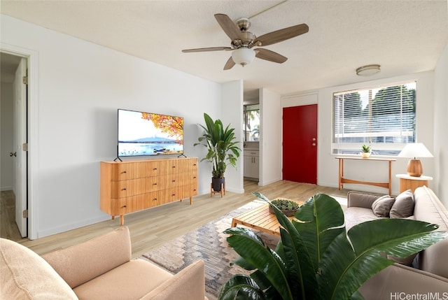 living room with ceiling fan, a textured ceiling, light wood-style flooring, and baseboards