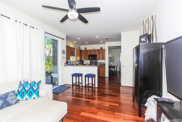 kitchen with black microwave, a breakfast bar area, recessed lighting, dark wood-type flooring, and brown cabinetry