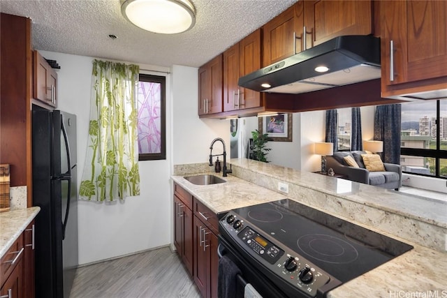 kitchen with a textured ceiling, light wood-style flooring, under cabinet range hood, a sink, and black appliances