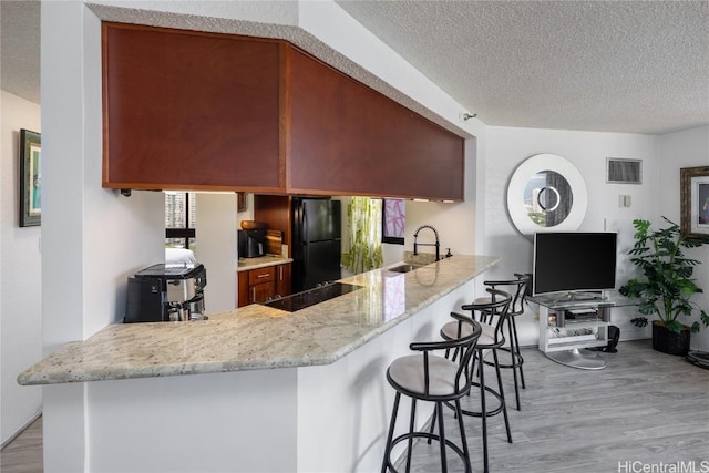 kitchen with a peninsula, a sink, visible vents, light wood-style floors, and black appliances