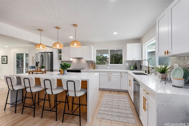 kitchen with a center island, pendant lighting, stainless steel refrigerator with ice dispenser, white cabinetry, and a sink