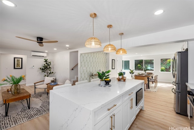 kitchen with a center island, pendant lighting, a wall unit AC, freestanding refrigerator, and white cabinets