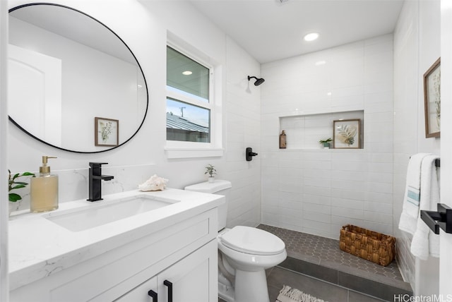 bathroom with toilet, tile patterned flooring, tiled shower, and vanity