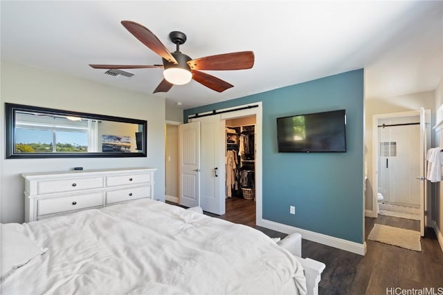 bedroom featuring a spacious closet, a barn door, visible vents, and dark wood-style flooring