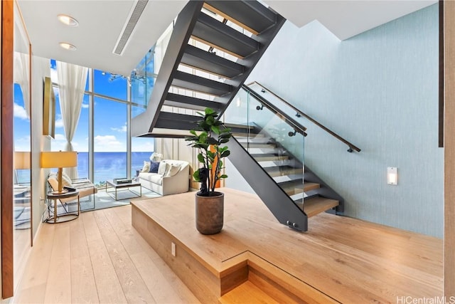 staircase featuring a wall of windows, a water view, and wood-type flooring