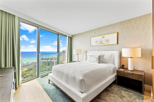 bedroom with access to exterior, floor to ceiling windows, a water view, and wood finished floors