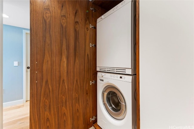 clothes washing area featuring baseboards, light wood-style floors, laundry area, and stacked washer / dryer