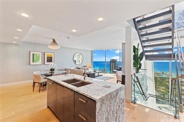 kitchen with a wall of windows, open floor plan, an island with sink, and light wood finished floors