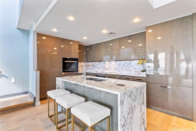 kitchen featuring visible vents, oven, light stone counters, light wood-style flooring, and modern cabinets