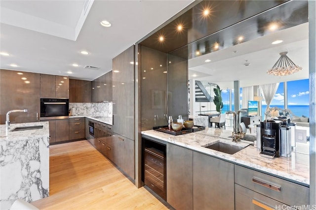 kitchen with oven, modern cabinets, beverage cooler, a sink, and light stone countertops