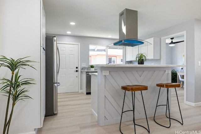 kitchen featuring island exhaust hood, stainless steel appliances, light countertops, light wood-style flooring, and white cabinets