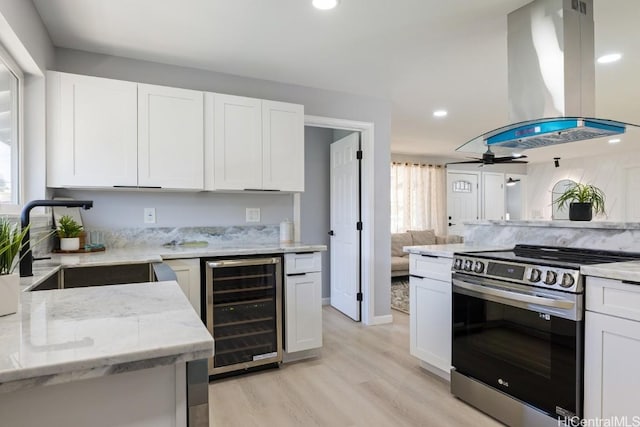 kitchen featuring electric range, island exhaust hood, white cabinetry, and beverage cooler