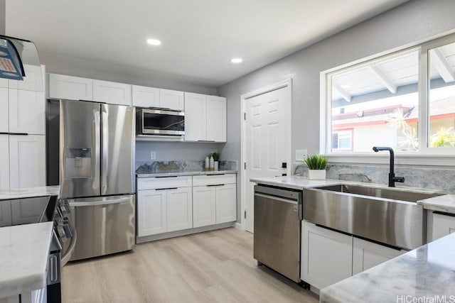 kitchen with light stone countertops, appliances with stainless steel finishes, white cabinets, and a sink