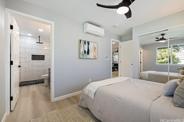 bedroom with light wood finished floors, a closet, ensuite bathroom, an AC wall unit, and baseboards