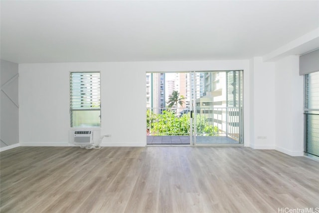 unfurnished room with light wood-style flooring, baseboards, and an AC wall unit