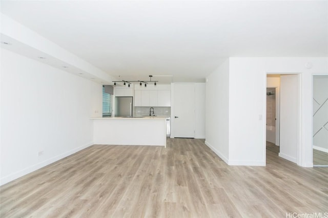 unfurnished living room featuring a sink, light wood-style flooring, and baseboards