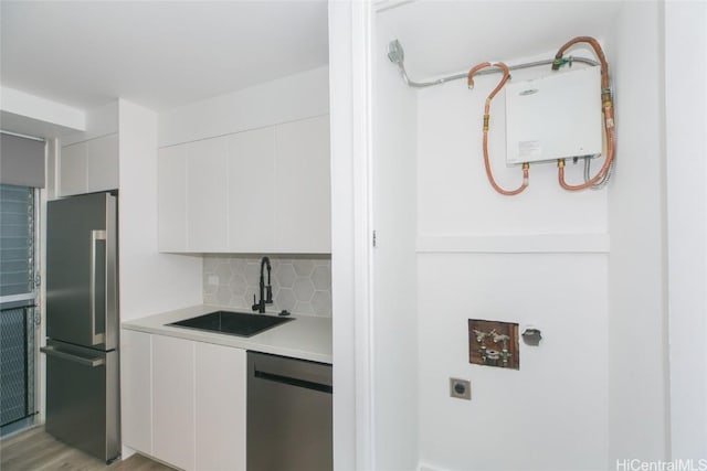 kitchen with white cabinets, a sink, stainless steel appliances, light countertops, and backsplash