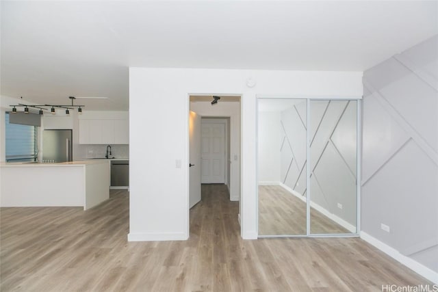 unfurnished living room with light wood-style floors, baseboards, a sink, and rail lighting