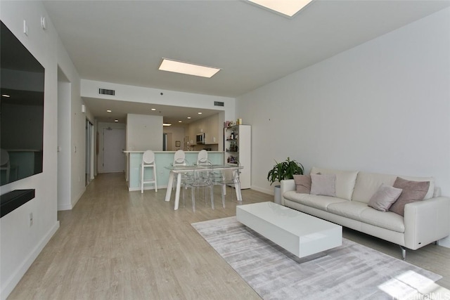 living area with light wood-type flooring, visible vents, and baseboards