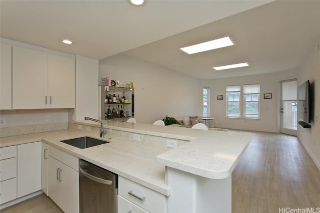 kitchen featuring open floor plan, a peninsula, stainless steel dishwasher, white cabinetry, and a sink