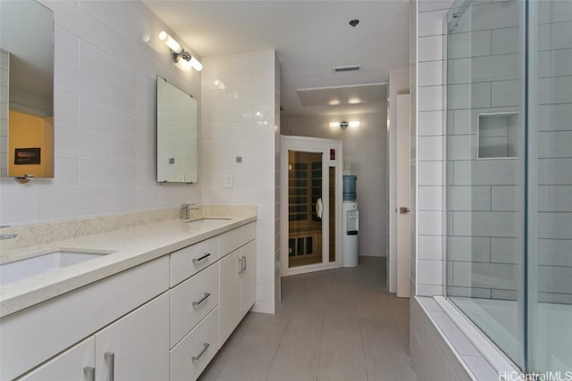 full bath featuring visible vents, tiled shower, a sink, and tile walls