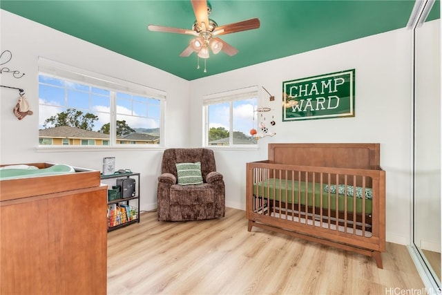 bedroom featuring a crib, wood finished floors, and a ceiling fan