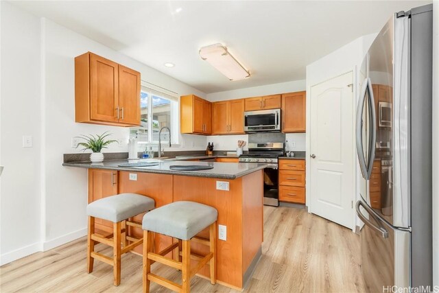 kitchen featuring a breakfast bar, light wood-style floors, appliances with stainless steel finishes, and a sink