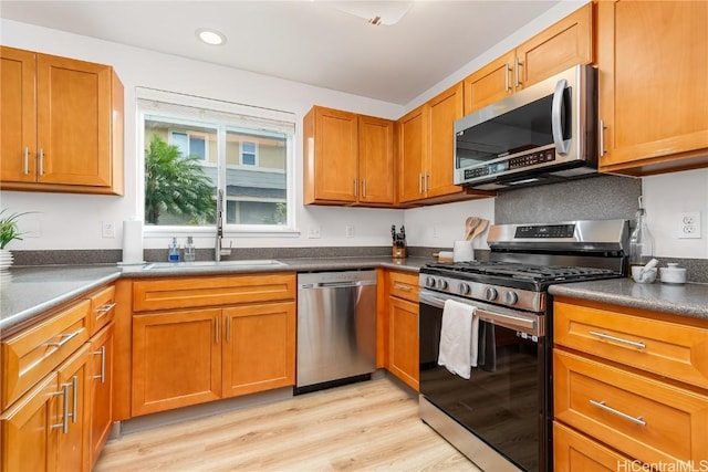 kitchen featuring dark countertops, light wood-style flooring, appliances with stainless steel finishes, and a sink