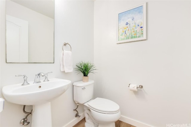 half bathroom with toilet, baseboards, and a sink