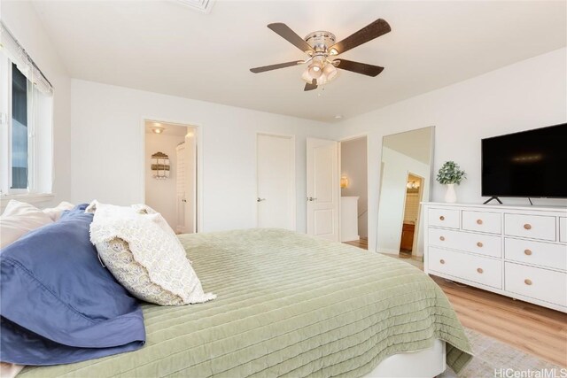 bedroom featuring light wood finished floors, ensuite bathroom, and a ceiling fan