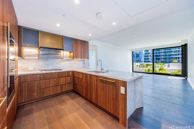 kitchen with a peninsula, wood finished floors, a sink, brown cabinetry, and modern cabinets