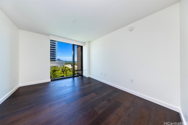 empty room featuring dark wood-type flooring, a wall of windows, and baseboards