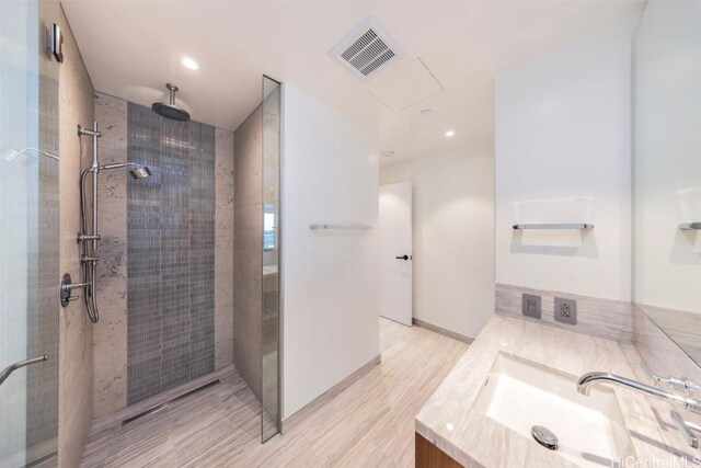 full bathroom with visible vents, a tile shower, and vanity