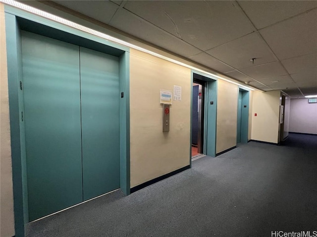 hall with elevator, baseboards, and a drop ceiling