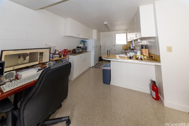 kitchen featuring a peninsula, white cabinets, light countertops, freestanding refrigerator, and concrete block wall