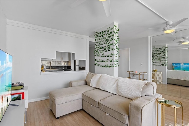 living area with light wood-style flooring, baseboards, and a ceiling fan