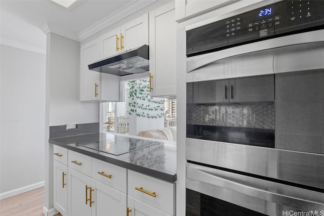 kitchen with stainless steel double oven, ornamental molding, under cabinet range hood, white cabinetry, and black electric stovetop