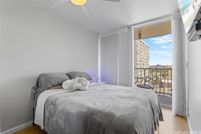 bedroom with a wall of windows, access to outside, wood finished floors, and baseboards