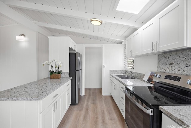 kitchen featuring beam ceiling, stainless steel appliances, light wood-style flooring, white cabinetry, and a sink