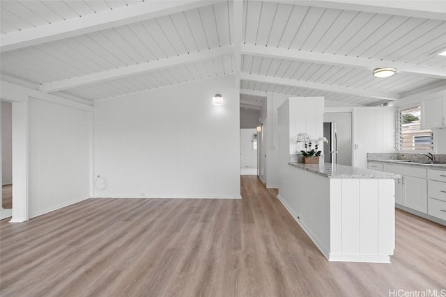 unfurnished living room with baseboards, a sink, light wood-style flooring, and lofted ceiling with beams