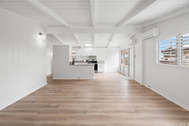 unfurnished living room featuring a wall unit AC, light wood finished floors, and beam ceiling