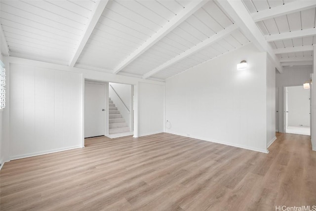 spare room featuring vaulted ceiling with beams, light wood finished floors, stairway, and baseboards