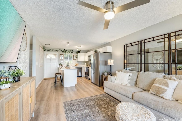 living room with a textured ceiling, light wood-type flooring, and a ceiling fan