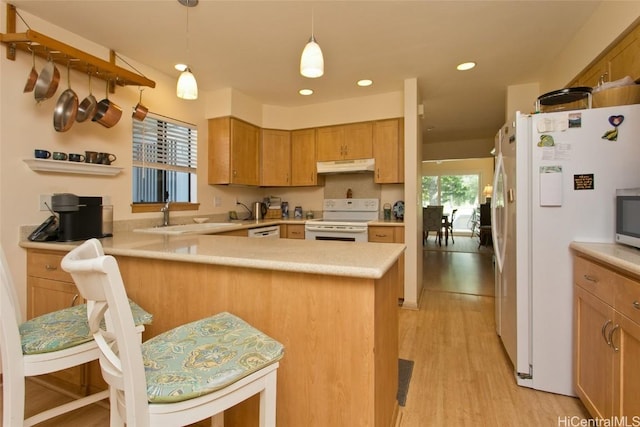 kitchen featuring light countertops, a sink, a peninsula, white appliances, and under cabinet range hood